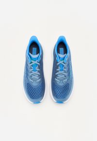 Baskets de sport bleues avec une tige en maille texturée, des lacets d'un bleu plus clair en contraste et une semelle en caoutchouc blanche, avec de subtils accents verts.