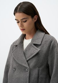Cappotto in misto lana grigio con design doppiopetto, colletto a punte, grandi bottoni e tasche laterali. Tessuto morbido e vestibilità su misura.