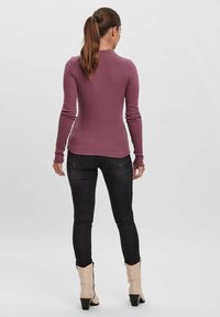 Langärmliges, geripptes Oberteil in gedämpftem Mauve, kombiniert mit engen, dunklen Jeans und Ankle Boots. Das Oberteil hat einen hohen Kragen und eine figurnahe Passform.