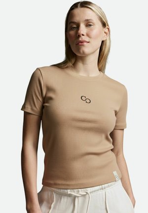 Beige geripptes T-Shirt mit kurzen Ärmeln, das ein kleines schwarzes Logo auf der Brust und ein Etikett an der Seite aufweist, aus einem weichen Stoff gefertigt.