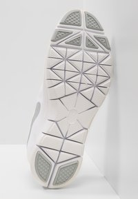 Sål af hvid atletisk sko med geometrisk mønster og grå teksturerede gummigrebindsatser på hælen og tåen.
