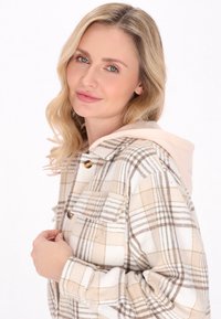 Rutiga skjortjacka i kräm- och brunt toner med en beige huva. Har två bröstfickor och guldtonade knappar. Mjuk, texturerad tät.