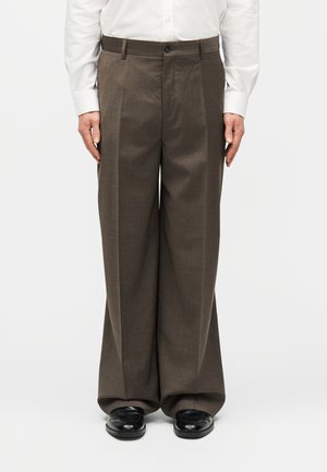 Καφέ ανδρικό παντελόνι με φαρδιά μπατζάκια, σε συνδυασμό με μαύρα επίσημα παπούτσια και λευκό πουκάμισο με μακριά μανίκια και κουμπιά.