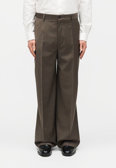 Pantalon ample marron pour homme associé à des chaussures habillées noires et une chemise blanche à manches longues et boutons.