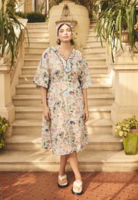 Šaty s květinovým vzorem, krátkými širokými rukávy a výstřihem do V. Světlé barvy a zúžený pas. Kombinovány s bílými žabkami.