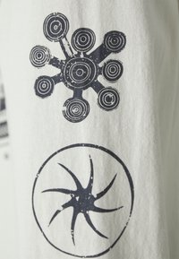 Tricou alb din bumbac cu două modele imprimate: un model circular cu cercuri concentrice și o formă asemănătoare unei stele, ambele în nuanțe de albastru închis.