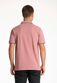 Kortärmad polo i ljusrosa bomull, med krage och ärmmuddar i svart och vitt randigt mönster. Slät textur, vanlig passform.