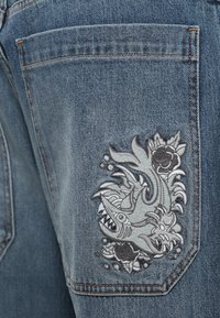 Plava traperica s džepom na ledu sa siva i crna izvezena designom morske pjene i cvjetovima.