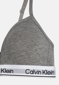 Szürke pamut bralette, háromszög alakú kosarakkal. Fehér pánttal rendelkezik, amelyen fekete "Calvin Klein" logo található, valamint állítható szürke pántokkal. Simma textúrával.