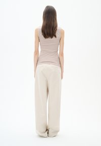 Canotta beige a coste abbinata a pantaloni larghi di un beige chiaro. Il modello è mostrato di spalle su uno sfondo bianco.