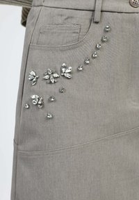 Tissu gris avec une texture subtile, orné d'embellissements décoratifs de pierres ressemblant à des cristaux dans des motifs floraux et dispersés.