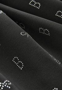 Un tissu noir présente une texture lisse, orné de strass transparents formant des lettres et des motifs éparpillés sur la surface.