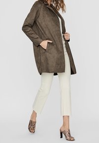 Ruskosuinen mokkatakki, jossa on kaulus ja sivutaskut, yhdistettynä vaaleanbeigeihin lyhyisiin housuihin ja kuviollisiin korkokenkiin.