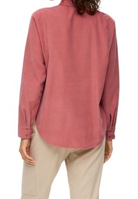 Roze langemouwen blouse van zachte stof, met een afgeronde zoom, knoopmanchetten en een rugpasdetail. Gepaard met lichtbeige broeken.