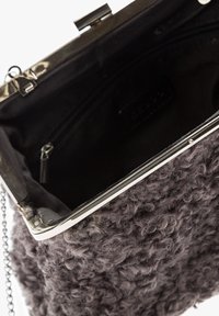 Sivi teksturirani ručni torba s mekanim, kovrčavim vanjskim dijelom. Ima srebrni metalni okvir i lančanu naramenicu, otvoren unutrašnji prostor s zip zatvaračem.