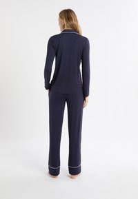 Completo da soggiorno blu navy con maniche lunghe, pantaloni coordinati e dettagli in piping bianco. Tessuto morbido con vestibilità rilassata e gambe a taglio dritto.