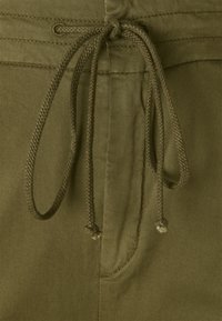 Olivově zelená látka s uzávěrem na šňůrku, charakterizovaná hladkou texturou a prošitými detaily kapes. Jednoduchý a funkční design.