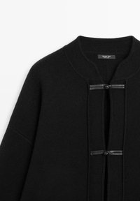 Cardigan nero lavorato a maglia con colletto rotondo, dotato di due dettagli in tessuto nero all'apertura frontale e di un'etichetta cucita all'interno del colletto.