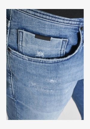 Jeans de mezclilla azul claro con un acabado desgastado, que cuentan con una etiqueta en el bolsillo trasero y costuras en contraste a lo largo de las costuras.