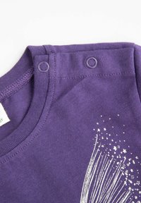 Fioletowa bawełniana koszulka z zapięciem na napy na ramieniu, z białym wzorem gwiazdy i linii na przodzie, gładka tekstura i okrągły dekolt.