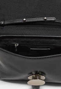 Sac à main noir avec un extérieur en cuir lisse, une fermeture magnétique et une poche intérieure zippée. Conception simple et fonctionnelle.
