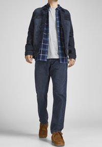Chaqueta de denim, superpuesta con una camisa de cuadros azules sobre una camiseta gris, combinada con pantalones azul oscuro y mocasines de ante marrón.
