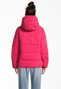 Rosa Pufferjacke mit Kapuze, ausgestattet mit gestepptem Textur und geometrischen Nähten. Das Model trägt hellblaue weit geschnittene Jeans.