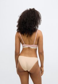 Lyserød BH med blonderkant, justerbare stropper og lukning bagpå; kombineret med beige sømløse trusser i tætsiddende stil.
