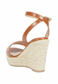 Sandalo con zeppa in pelle verniciata marrone, con cinghie incrociate alla caviglia e un tacco in juta testurizzata, caratterizzato da una punta tonda e un design aperto sul retro.