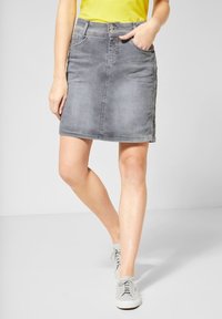 Grå denimkjol med en åtsittande form, mitt på låret längd, framfickor och knäppning med knapp. Matchad med en gul topp och grå sneakers.