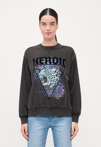 Svart genser med hette med en triangulær leopardgrafikk med multicolor aksenter. Ribbestrikkede mansjetter og nederkant med en avslappet passform.