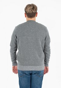 Maglione grigio lavorato a maglia con collo rotondo e maniche lunghe. Presenta un orlo e polsini a coste, mostrando una texture morbida. Indossato con jeans blu.