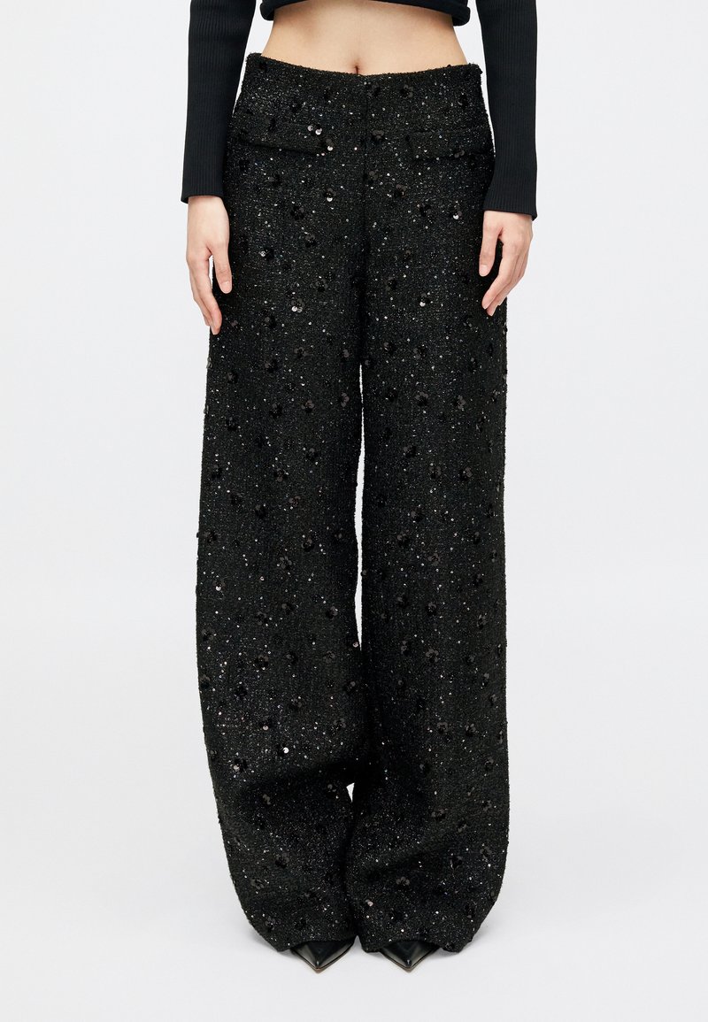Pantalons larges en tissu noir avec une surface texturée agrémentée de sequins. Poches avant et coupe droite du taille à l'ourlet.