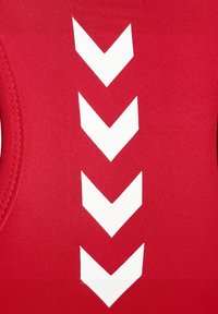 Witte naar beneden wijzende chevrons in een verticale lijn op felrood gestructureerd textiel.