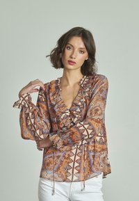 Blusa a fantasia con scollatura ruffle e maniche lunghe. Presenta un motivo paisley arancione, blu e crema con dettagli a cordoncino.