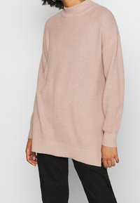 Pullover overdimensionato in maglia di colore rosa chiaro, con colletto alto, texture a coste e maniche lunghe. Caratterizzato da un orlo dritto e una vestibilità morbida.