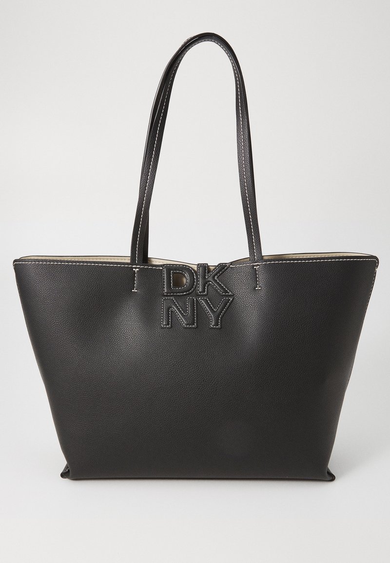 Black leather tote bag with a textured finish, featuring a logo emblem in the center and contrasting stitching. Two long handles for carrying.