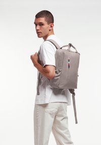 Grå ryggsäck med rektangulär form, texturerad yta och framficka med dragkedja. Justerbara remmar och handtag på toppen för mångsidig bärkomfort.