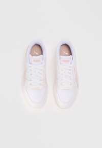 White athletic shoes with light pink accents, featuring a textured upper, lace closure, and a rubber sole. Logo appears on the tongue and side.