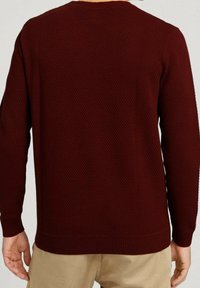 Bordowy sweter dziany z fakturowanym wzorem, długimi rękawami oraz ściągaczami przy mankietach i u dołu. Posiada okrągły dekolt i luźny krój.