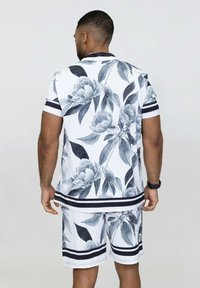 Ensemble deux pièces à manches courtes mettant en avant un tissu blanc orné de motifs floraux gris, rehaussé de rayures noires sur le col et le short.