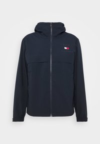 Giacca a vento blu navy con zip frontale, cappuccio e polsini elasticizzati. Presenta un logo sul petto e una texture semplice e liscia.