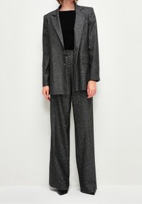 Completo grigio a quadri con una vestibilità ampia, caratterizzato da particelle argentate. Il blazer ha delle ampie revers e due bottoni. Abbinato a pantaloni dritti.