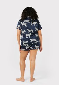 Kortärmad pyjamas i marinblått tyg med zebramönster, med röda detaljer på ärmar och shorts, som har en mjuk textur och avslappnad passform.