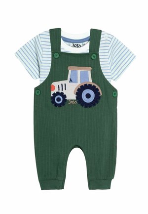 Grüne gerippte Latzhose mit blauen Knöpfen und einem Traktor-Design. Kombination mit einem hellblau-weißen Streifen-T-Shirt darunter.