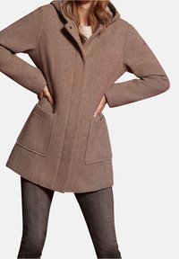 Cappotto marrone con texture e cappuccio, dotato di due tasche frontali e una vestibilità sartoriale. Il tessuto presenta un motivo a coste per un interesse visivo aggiunto.