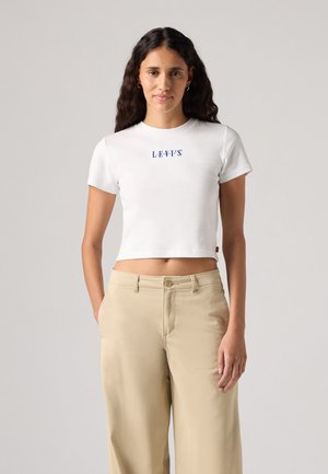 Biała krótka koszulka z krótkim rękawem, z niebieskim napisem "LEVI'S" na środku. Połączona z jasnobeżowymi spodniami typu wide-leg.