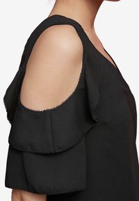 Schwarzes Top mit kalten Schultern und geschichteten Rüschensäumen, das mit gewellten Kanten und einer glatten Stofftextur begeistert.