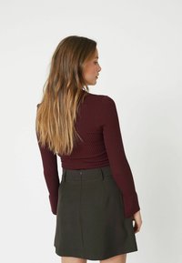 Ribbed maroon long-sleeve top paired with a dark green A-line skirt, featuring a zipper closure and tailored fit.
