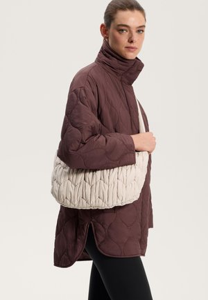 Veste matelassée de couleur bourgogne profonde avec un col montant. Associée à un sac à épaule bouffant de couleur crème présentant un motif texturé.
